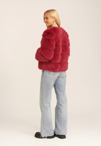 Red faux fur jacket with horizontal stitching, round collar, and side pockets. Paired with light blue flared jeans and black platform shoes.