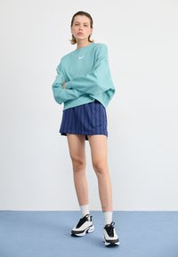 Lichtblauwe oversized sweatshirt, marineblauwe gestreepte shorts, wit en zwarte sneakers, die een ontspannen pasvorm en gelaagde texturen laat zien.