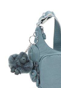 Teal tygaxelväska med dragkedjefack, prydd med en mjuk gorillanyckelring och silverfärgad hårdvara. Texturerat, hållbart material.