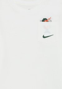T-shirt bianco in cotone con tasca, caratterizzato da una grafica di cartone animato. Include un logo Nike verde ricamato sulla tasca. Collo rotondo.