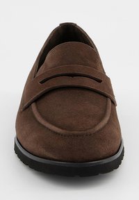 Mocassin en daim marron avec une semelle en caoutchouc noire, un bout arrondi et une bride sur le dessus, vu de face.