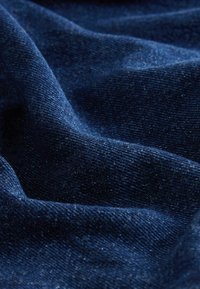 Tumši jūras zilas denima audums ar gludu tekstūru, ar smalkiem zilajiem apakškārtām un mīkstu, austu apdari. Materiāls dabiski krīt krokās.