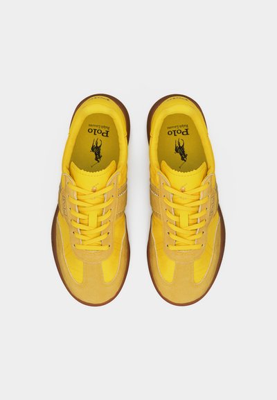 Ζευγάρι κίτρινων αθλητικών παπουτσιών Polo Ralph Lauren με καφέ σόλες, σχέδιο με κορδόνια και λογότυπο τυπωμένο στις μαξιλαρωτές εσωτερικές σόλες, φωτογραφημένα από πάνω.