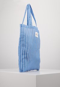 Niebieska torba tote w paski z długimi uchwytami, wykonana z gładkiego materiału. Posiada prostokątną metkę z boku. Prosty, funkcjonalny design.