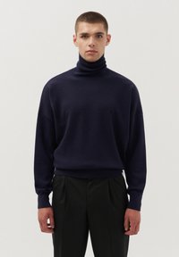 Granatowy sweter z golfem wykonany z miękkiej przędzy, charakteryzujący się luźnym krojem, długimi rękawami i prążkowanymi mankietami, w połączeniu z czarnymi spodniami.