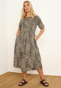 Sukienka w panterkę z krótkimi rękawami, dekoltem w kształcie klucza, marszczonym dołem, kieszeniami, wykonana z lekkiego materiału, zestawiona z brązowymi sandałami.