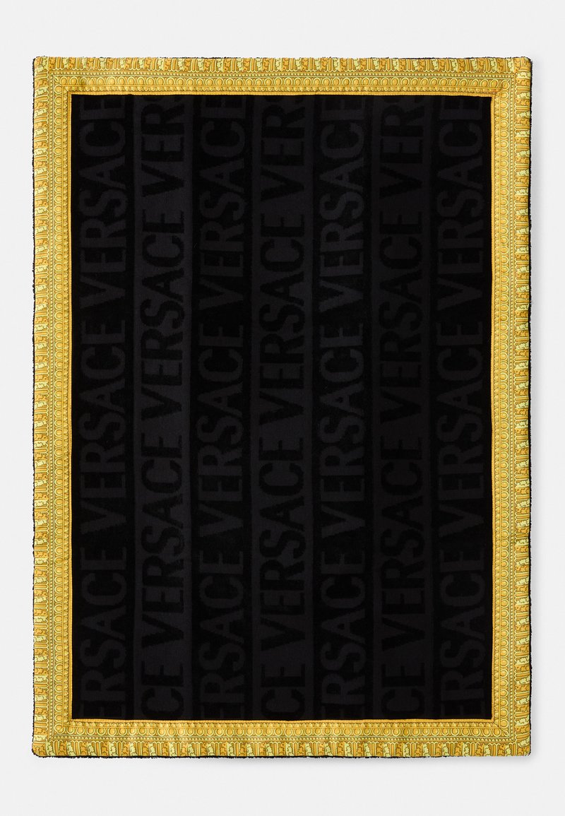 Črn material z večkrat ponovljenim logotipom "VERSACE", obkrožen s prefinjenim zlatim okvirom z zapletenimi podrobnostmi in teksturo.