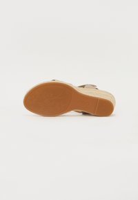 Brown espadrille sandal with a woven rope platform and rubber outsole, featuring a floral pattern on the bottom for traction.