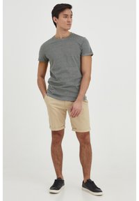 Tricou gri cu mânecă scurtă, pantaloni scurți bej răsuciți, adidași negri. Țesătura pare netedă, cu o croială lejeră, având un design simplu și fără modele vizibile.