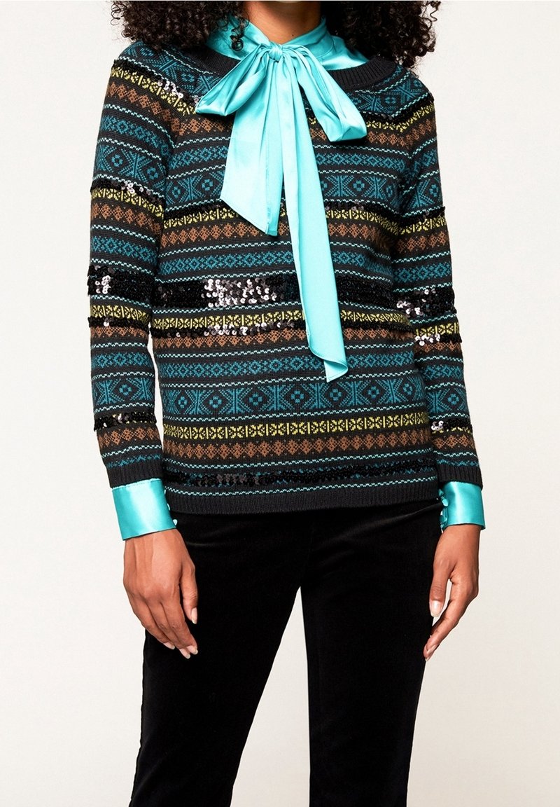 Wielokolorowy sweter z dzianiny z geometrycznym wzorem, czarna baza i turkusowy satynowy kołnierzyk z kokardą. Cekiny dodają tekstury i blasku.
