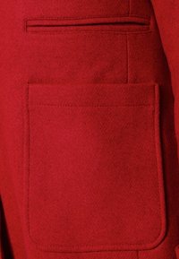Tela de abrigo de lana roja con un gran bolsillo de parche cuadrado de textura suave. Costuras decorativas corren a lo largo del lado del bolsillo.