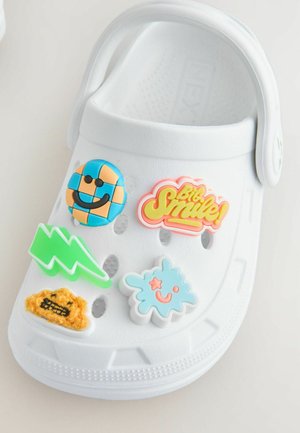 Crocs bianchi decorati con charm colorati che presentano una faccina sorridente, un fulmine e design di nuvole giocose.