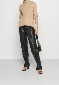 Beiger, gerippter Rollkragenpullover, kombiniert mit schwarzen Lederhosen mit ausgestellten Bündchen und schmaler Passform sowie schwarzen Sandaletten mit Absatz.