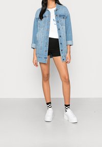 Lyseblå denimjakke med knappelukning, parret med en hvid t-shirt, sorte shorts og hvide sneakers med ternede sokker.