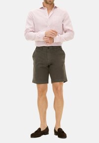 Camicia a righe rossa e bianca, pantaloni corti verdi scuri e mocassini marroni. La camicia ha maniche lunghe e una tasca sul petto. I pantaloni corti sono lunghi fino al ginocchio.