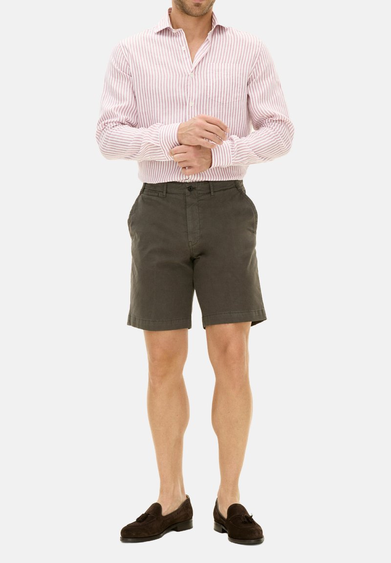 Camicia a righe rossa e bianca, pantaloni corti verdi scuri e mocassini marroni. La camicia ha maniche lunghe e una tasca sul petto. I pantaloni corti sono lunghi fino al ginocchio.