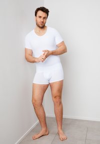 White cotton short-sleeve fitted top and matching boxers. Smooth texture, minimal design, and stretchy waistband. Barefoot on a tiled surface.