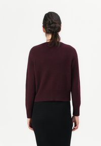 Suéter borgonha com um design cropped, mangas longas e punhos canelados, combinado com uma saia preta. Textura suave e detalhes minimalistas.