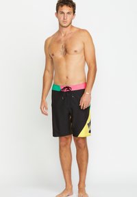 Shorts de bain noirs avec une ceinture multicolore aux accents rose, vert et noir, et des motifs graphiques jaunes sur le côté.