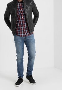 Black leather jacket over a red and blue checkered shirt, paired with light blue jeans and black sneakers. Casual outfit with contrasting textures.