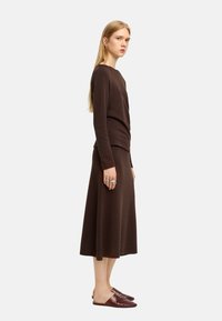 Brązowy sweter i spódnica w zestawie z miękkiego dzianiny, z dopasowaną górą i spódnicą w kształcie litery A, zestawione z brązowymi butami wsuwanymi. Minimalistyczny design.