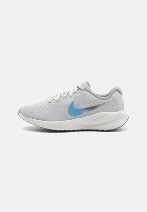 Zapatilla deportiva gris claro con parte superior de malla, logo azul, acentos texturizados y suela acolchada, con una puntera redondeada y cordones planos.