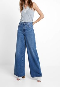 Szerokie, niebieskie dżinsy z wysokim stanem, z kontrastowym przeszyciem i kieszeniami po bokach, zestawione z jasnoszarym, bezrękawnikowym topem.