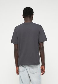 Tumši pelēks kokvilnas T-krekls ar apaļu kakla izgriezumu un īsām piedurknēm, ar tiešu apakšmalu. Gluda tekstūra, minimāls dizains.