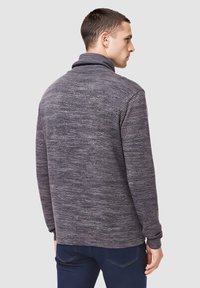 Camiseta gris de manga larga con textura, con cuello alto y sutiles rayas horizontales, mostrada desde atrás con mangas ajustadas.