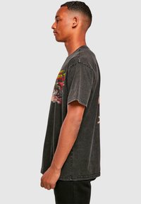 Sort, oversized bomulds T-shirt med en falmet finish og korte ærmer. Har et farverigt grafisk design på forsiden.