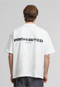 Weißes, übergroßes T-Shirt mit einem auffälligen schwarzen Aufdruck "VERBOTEN" und "10119, BERLIN" darunter, mit lockerer Passform und kurzen Ärmeln.