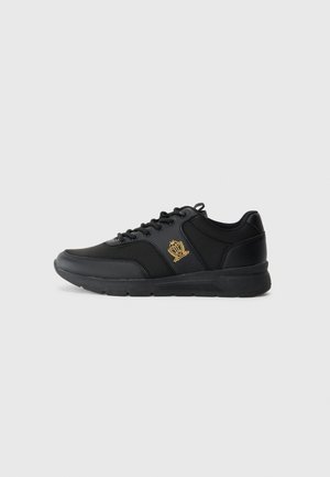 Black sneakers made of synthetic material with a smooth texture, featuring a gold logo detail, round toe, and lace-up design.