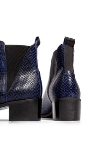 Niebieskie botki kostkowe w wzór węża z błyszczącym wykończeniem, elastycznymi panelami bocznymi i niskim czarnym obcasem w formie bloku. Gładka tekstura z wzorzystymi detalami.