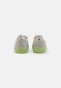 Sneakers with a grey synthetic upper, silver accents, and a translucent green rubber sole. Features a rounded toe and stitched detailing.