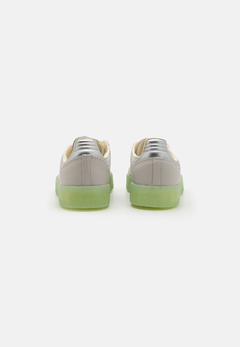 Sneakers con una parte superiore sintetica grigia, accentuazioni argentate e una suola in gomma traslucida verde. Presentano una punta arrotondata e dettagli cuciti.