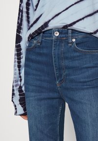 Blue denim jeans with a straight fit, featuring five-pocket design and contrast stitching. The waistband has a metal button and zipper closure.