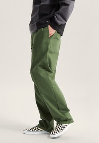 Zielone luźne spodnie wykonane z wytrzymałej bawełny. Do tego czarno-białe wsuwane buty w kratkę. Pozioma bluza w czarno-szare paski.