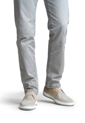 Beiget liukuvilla kengillä, joissa on teksturoitu kangas, kontrastiväriset ruskeat yksityiskohdat ja vaaleat kumipohjat. Päällä vaaleanharmaat farkut.