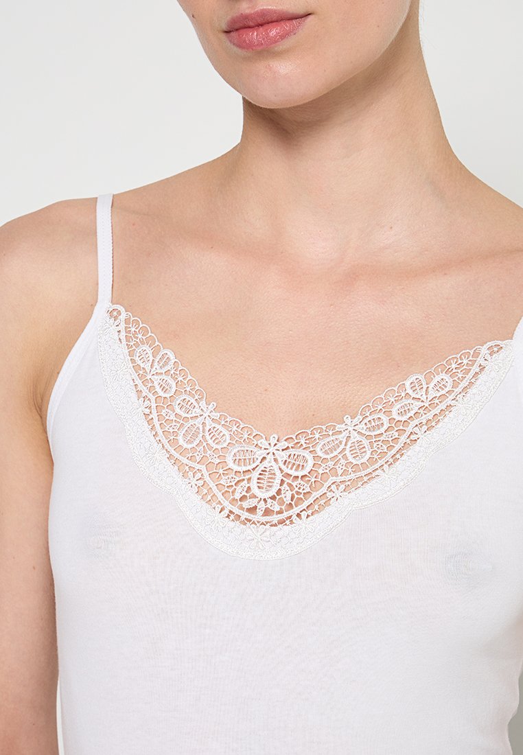 Weißes Top mit zarter weißer Spitzenborte entlang des V-Ausschnitts. Der Stoff ist leicht und glatt, ideal zum Schichten.