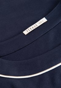 Tessuto morbido di colore blu navy presenta un collo rotondo con un accentuazione in piping bianco. Etichetta con la scritta "FÉRAUD PARIS." Texture liscia.