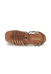 Sandal de cuero marrón con una suela plana, que presenta múltiples correas, una correa para el tobillo con hebilla y un diseño de puntera redonda.