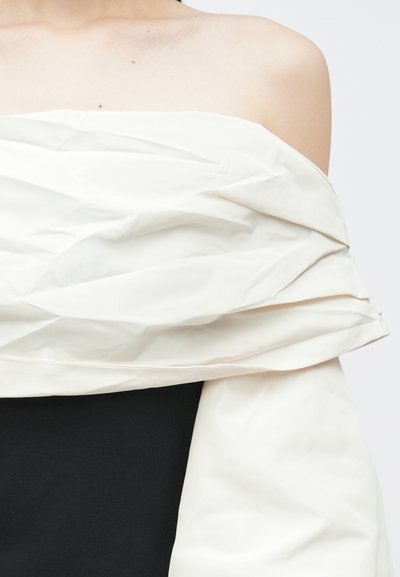 Top bez naramenica s strukturalnim, naboranim bijelim prekrivnim materijalom i uskim crnim donjim slojem, koji prikazuje kontrastne teksture.