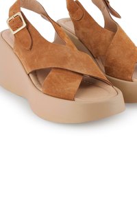 Sandalias de plataforma de ante marrón con tiras cruzadas, hebilla ajustable y una base beige sólida. Superficie texturizada y diseño de punta abierta.