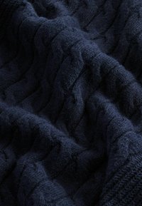 Tissu tricoté bleu foncé avec un motif texturé de points en relief, ondulés et entrelacés en forme de câble.