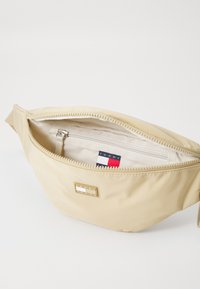 Marsupio in nylon beige con scomparto principale con zip, tasca interna e finiture dorate che presentano il logo del marchio sulla parte anteriore.