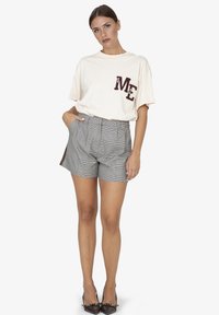 Cremefarbenes T-Shirt mit kurzen Ärmeln und dunkelroter "ME"-Aufschrift; graue und schwarze karierte Shorts mit hoher Taille; glatte Textur; modische spitze Absatzschuhe.