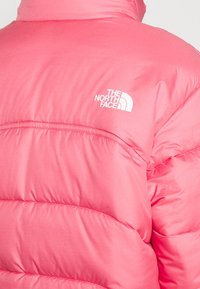 Giacca puffer rosa con design trapuntato. Presenta un colletto alto, dettagli cuciti e un logo bianco sulla spalla sinistra.