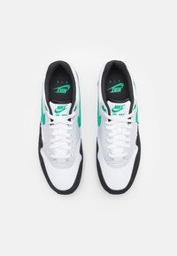 Baskets Nike Air Max avec une tige en mesh blanc, des accents gris, une semelle en caoutchouc noir et des détails de logo verts. Design classique à lacets.