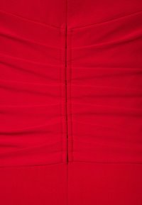 Robe rouge avec fronces horizontales en tissu texturé. La couture au centre du dos avec un détail de couture vertical met en valeur la silhouette.