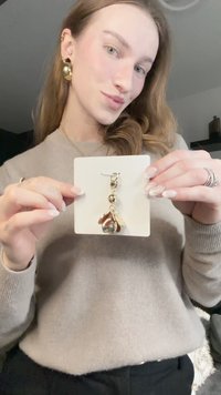 Gold-tone earrings featuring a textured drop design, adorned with a round bead and leaf-like accents, displayed on a white card.